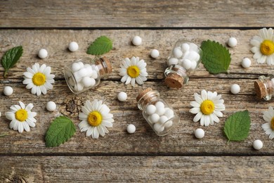 Homeopathic remedy. Many pills, bottles and chamomile flowers on wooden table, above view