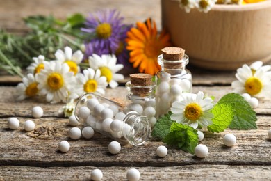 Homeopathic remedy. Many pills, bottles and chamomile flowers on wooden table, closeup