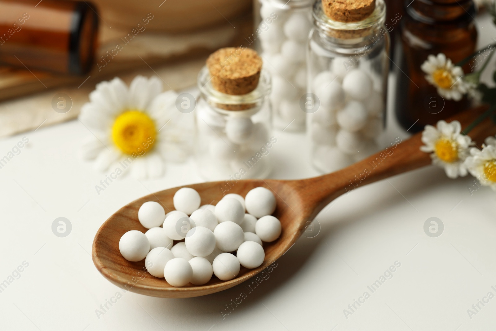 Photo of Homeopathic remedy. Spoon with pills, bottles and chamomile flowers on white table, closeup