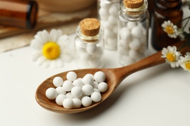 Homeopathic remedy. Spoon with pills, bottles and chamomile flowers on white table, closeup