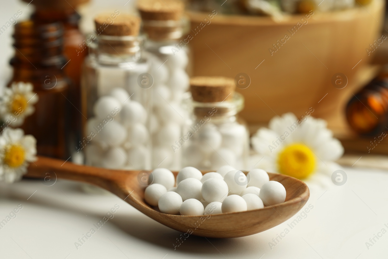 Photo of Homeopathic remedy. Spoon with pills, bottles and chamomile flowers on white table, closeup