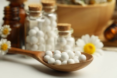 Photo of Homeopathic remedy. Spoon with pills, bottles and chamomile flowers on white table, closeup