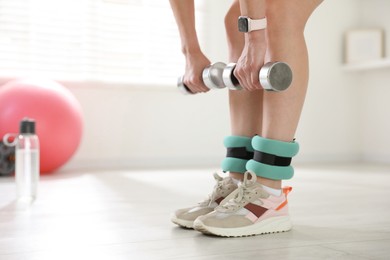 Photo of Woman with ankle weights and dumbbells training indoors, closeup