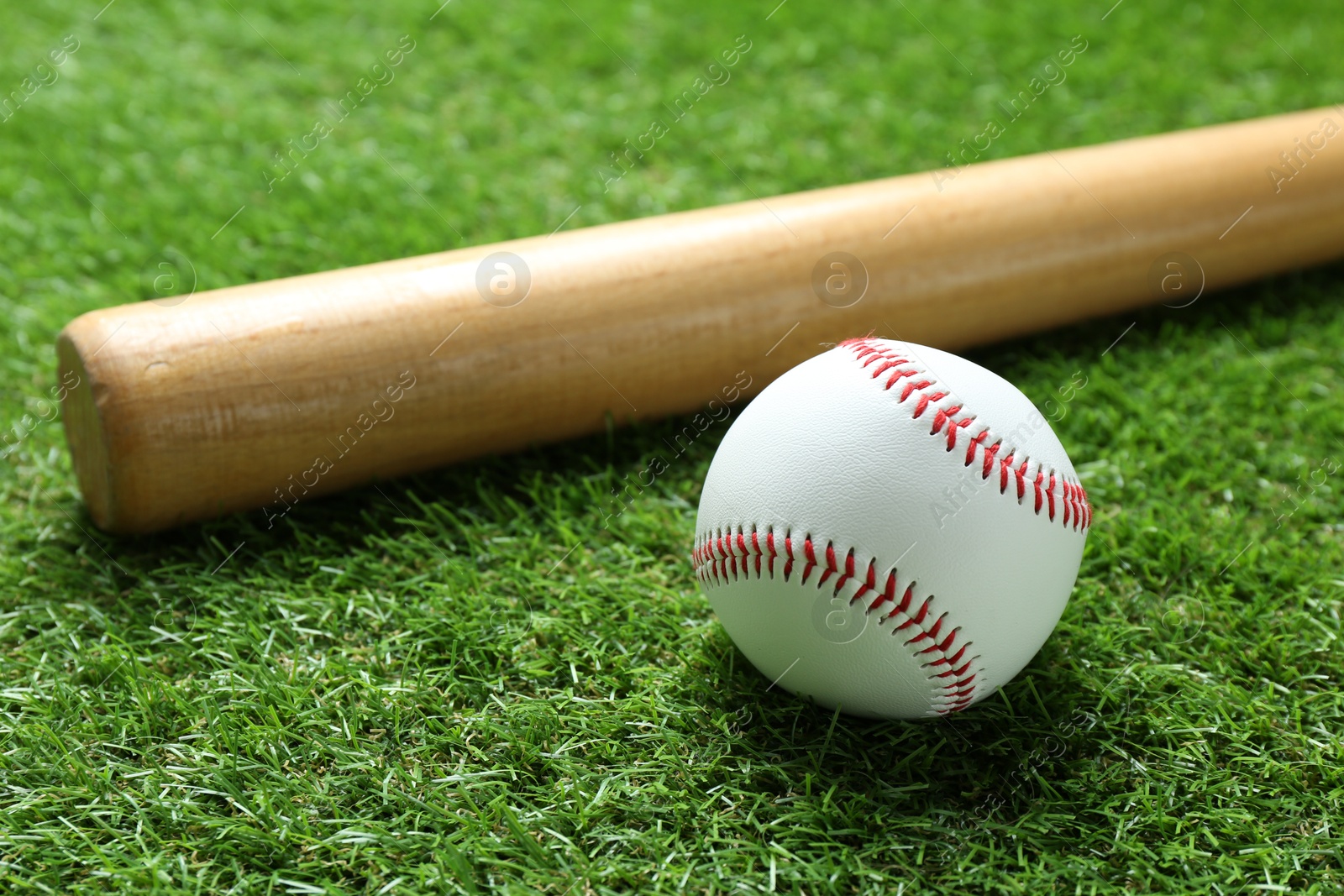 Photo of Baseball ball and bat on green grass outdoors, closeup