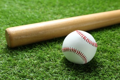 Photo of Baseball ball and bat on green grass outdoors, closeup