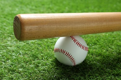 Photo of Baseball ball and bat on green grass outdoors, closeup