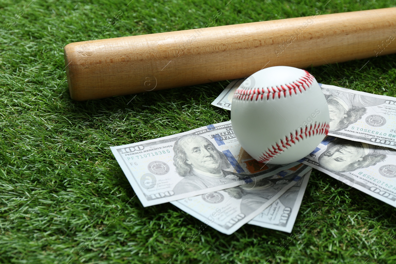 Photo of Baseball ball, bat and dollar banknotes on green grass outdoors