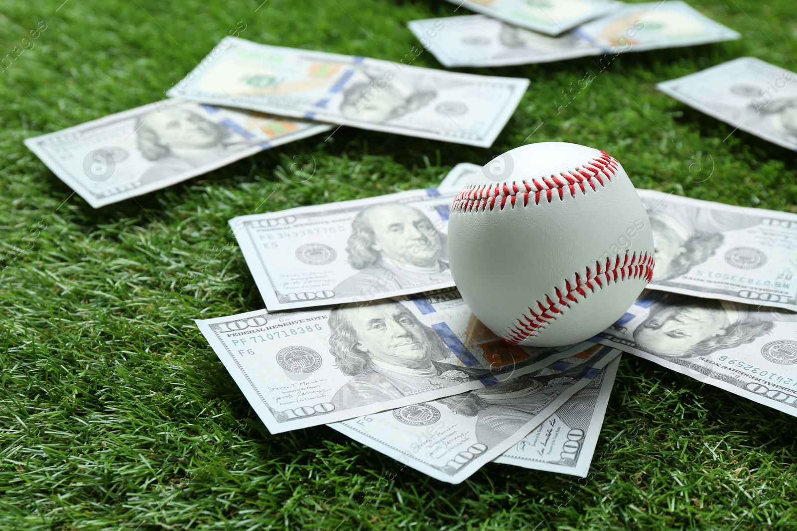 Photo of Baseball ball and dollar banknotes on green grass outdoors