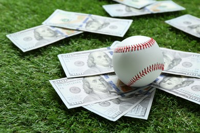 Photo of Baseball ball and dollar banknotes on green grass outdoors