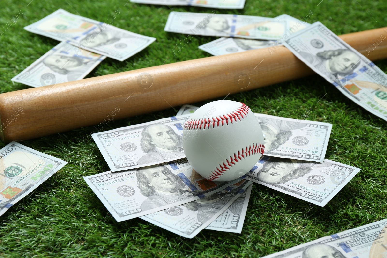 Photo of Baseball ball, bat and dollar banknotes on green grass outdoors