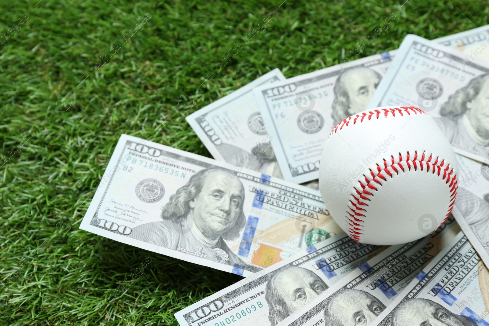 Photo of Baseball ball and dollar banknotes on green grass outdoors, closeup