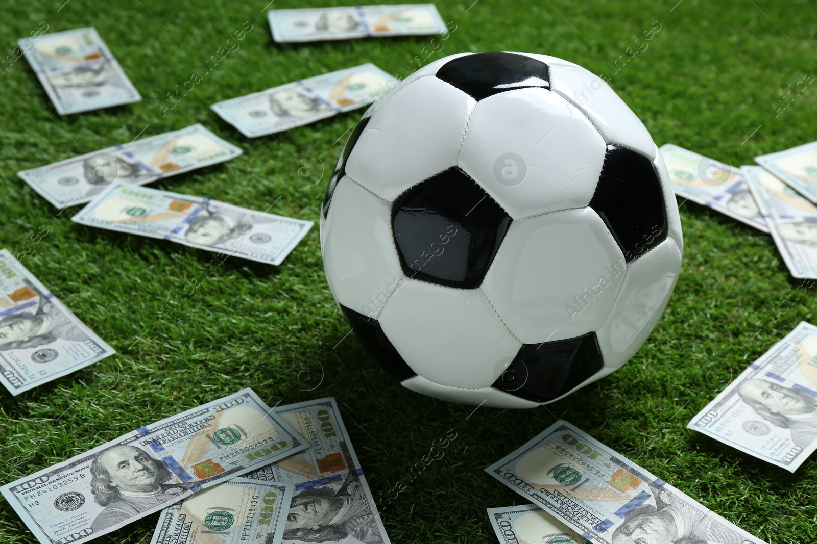 Photo of Soccer ball and dollar banknotes on green grass outdoors