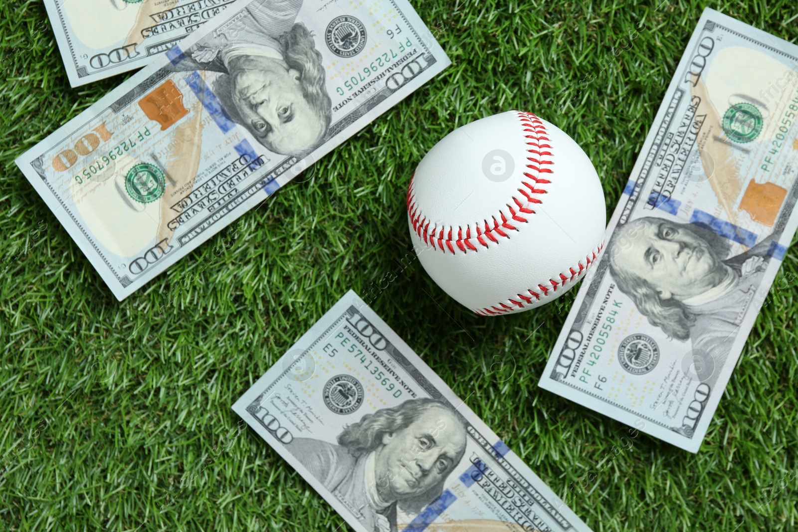 Photo of Baseball ball and dollar banknotes on green grass outdoors, flat lay