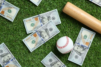 Photo of Baseball ball, bat and dollar banknotes on green grass outdoors, flat lay