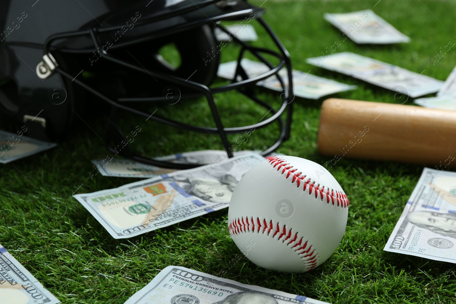 Photo of Baseball ball, bat, helmet and dollar banknotes on green grass outdoors, closeup