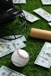 Photo of Baseball ball, bat, helmet and dollar banknotes on green grass outdoors