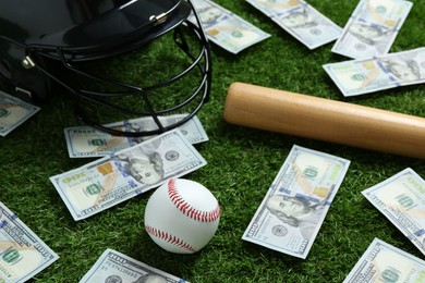 Photo of Baseball ball, bat, helmet and dollar banknotes on green grass outdoors