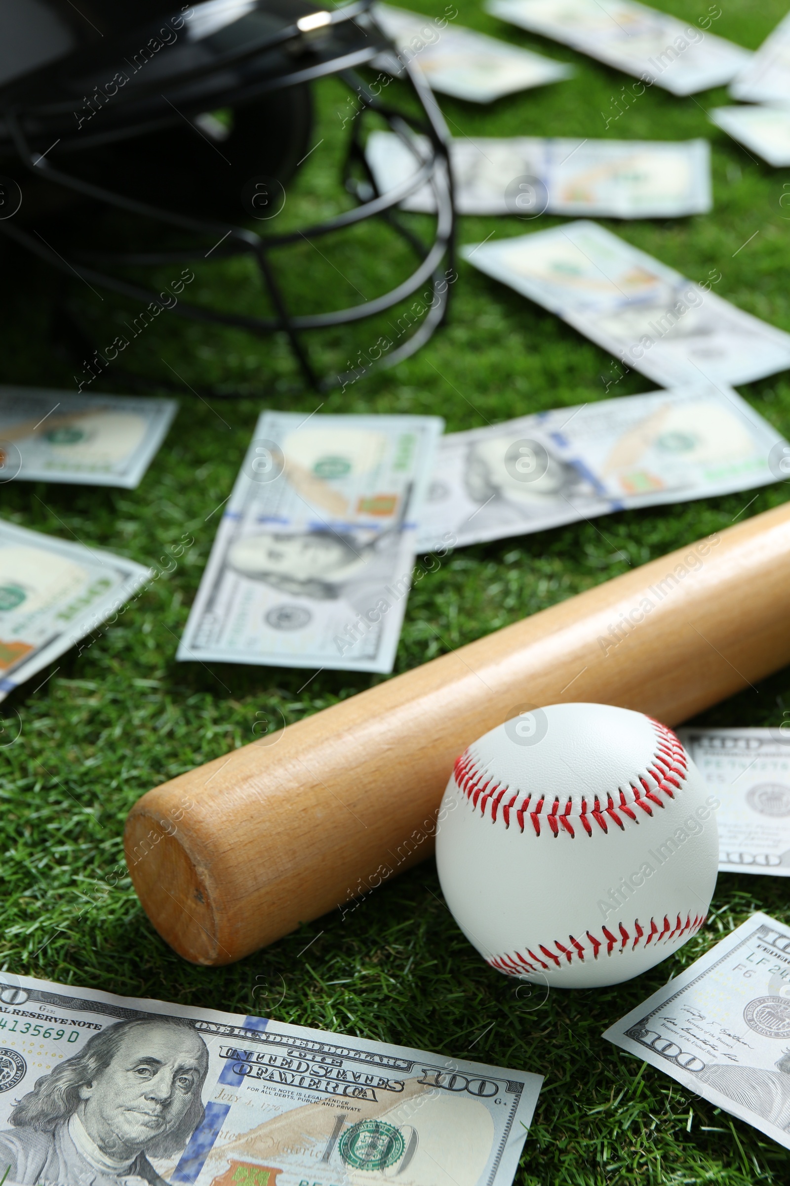 Photo of Baseball ball, bat, helmet and dollar banknotes on green grass outdoors