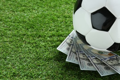 Photo of Soccer ball and dollar banknotes on green grass outdoors, space for text