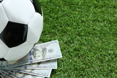 Photo of Soccer ball and dollar banknotes on green grass outdoors, closeup. Space for text