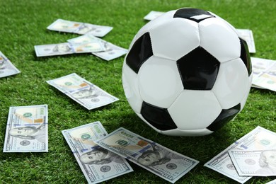 Photo of Soccer ball and dollar banknotes on green grass outdoors