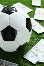 Photo of Soccer ball and dollar banknotes on green grass outdoors, closeup