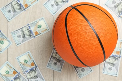 Photo of Basketball ball and dollar banknotes on wooden table, top view