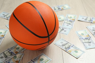 Photo of Basketball ball and dollar banknotes on wooden table, closeup