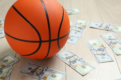 Photo of Basketball ball and dollar banknotes on wooden table, closeup