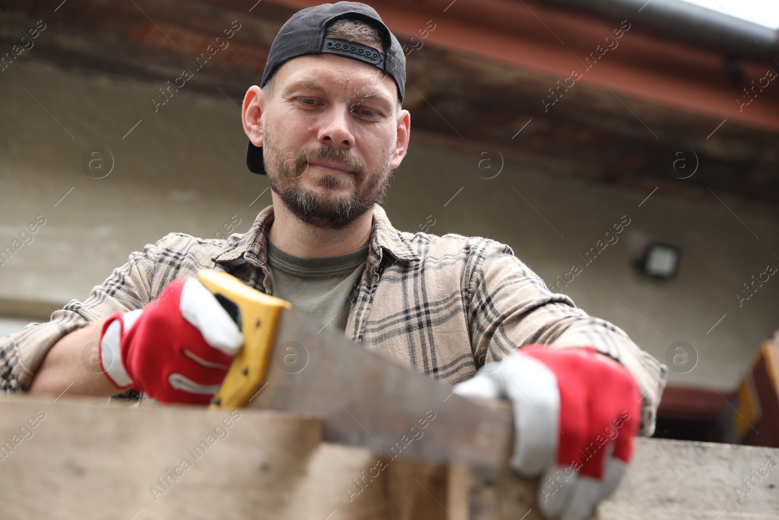 Photo of Handsome man sawing wooden plank in backyard