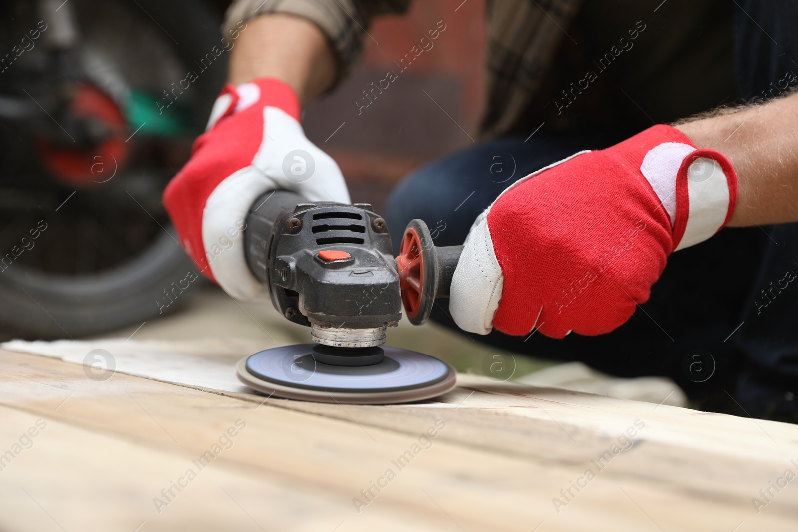 Photo of Man polishing wooden planks with angle grinder outdoors, closeup