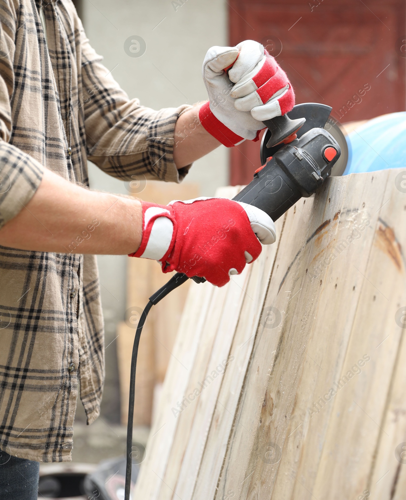 Photo of Man grinding wooden planks with angle grinder outdoors