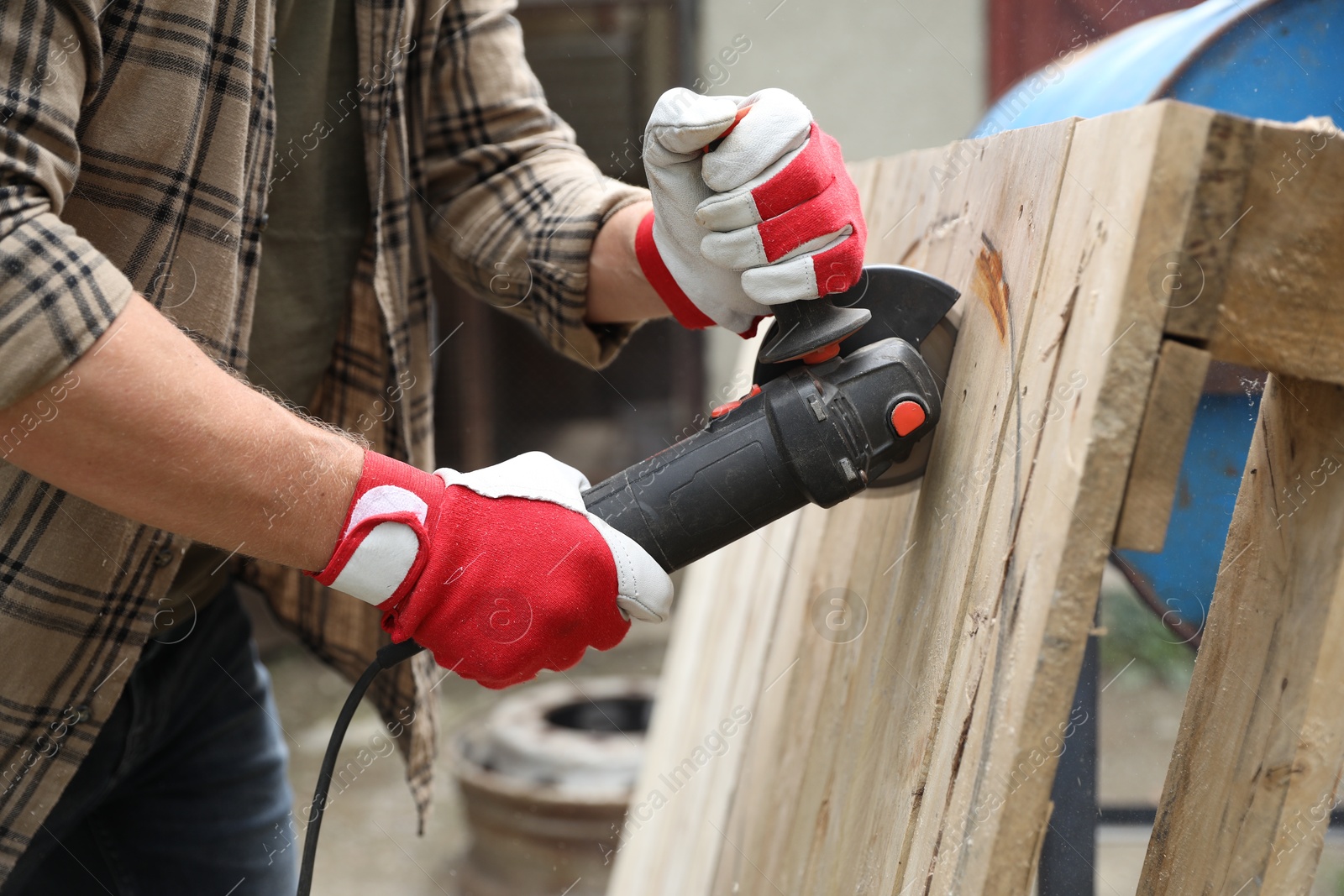 Photo of Man grinding wooden planks with angle grinder outdoors, closeup