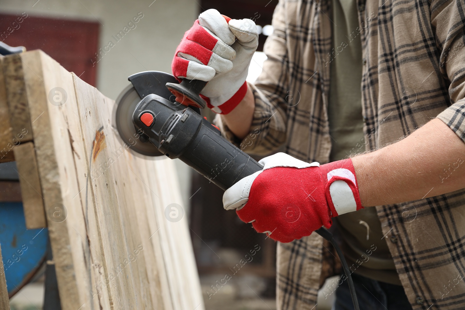 Photo of Man grinding wooden planks with angle grinder outdoors, closeup