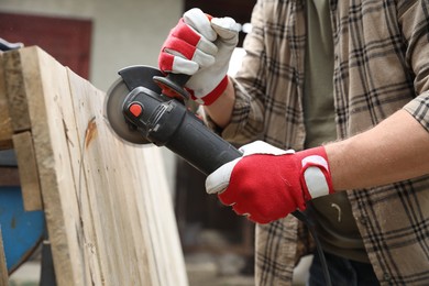 Photo of Man grinding wooden planks with angle grinder outdoors, closeup