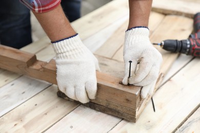 Photo of Man holding nail near wooden plank outdoors, closeup