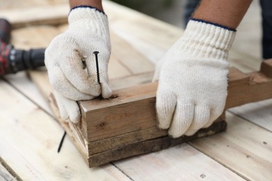 Photo of Man holding nail near wooden plank outdoors, closeup