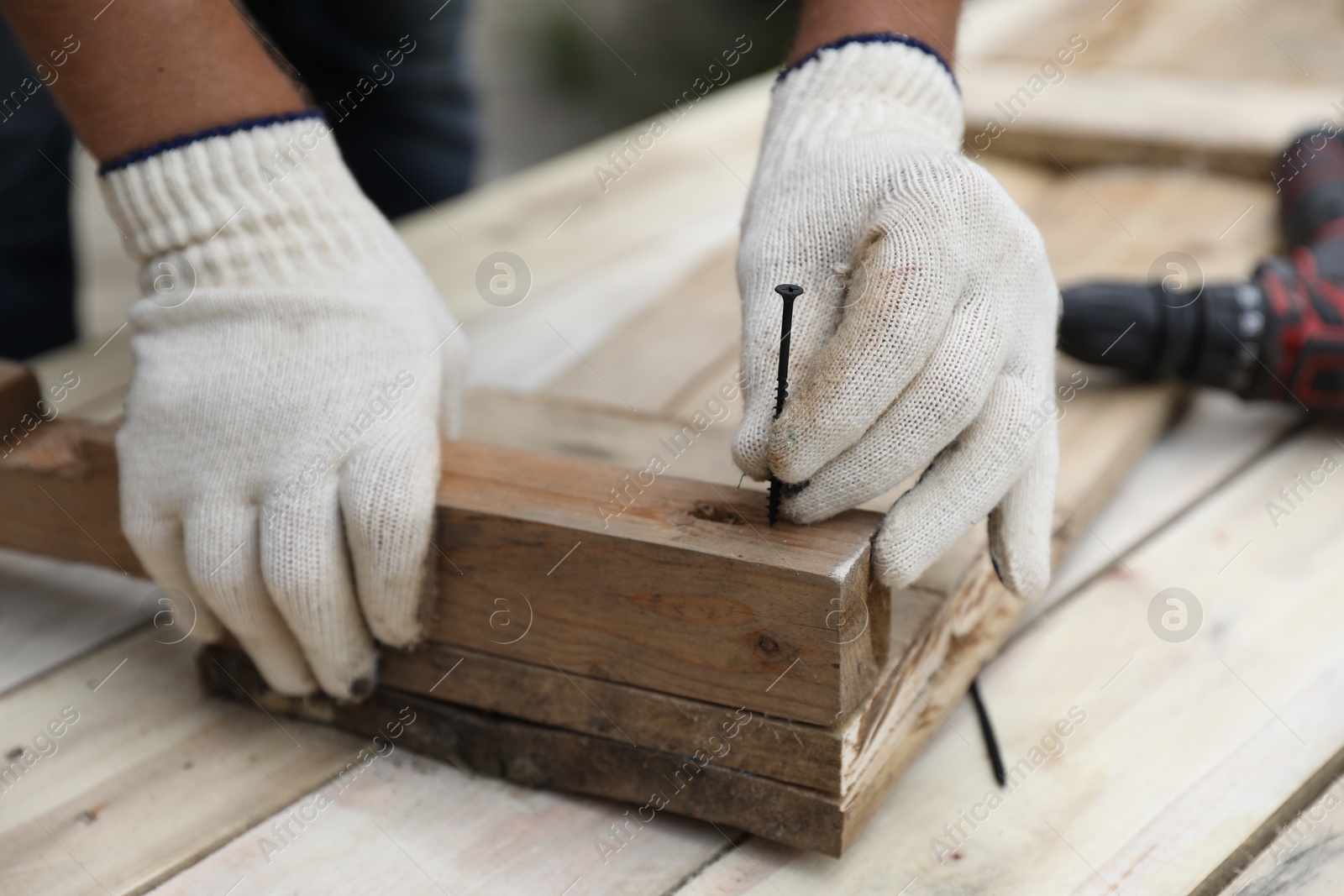 Photo of Man holding nail near wooden plank outdoors, closeup