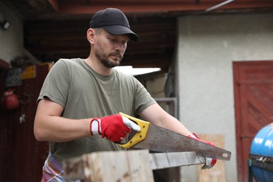 Handsome man sawing wooden plank in backyard