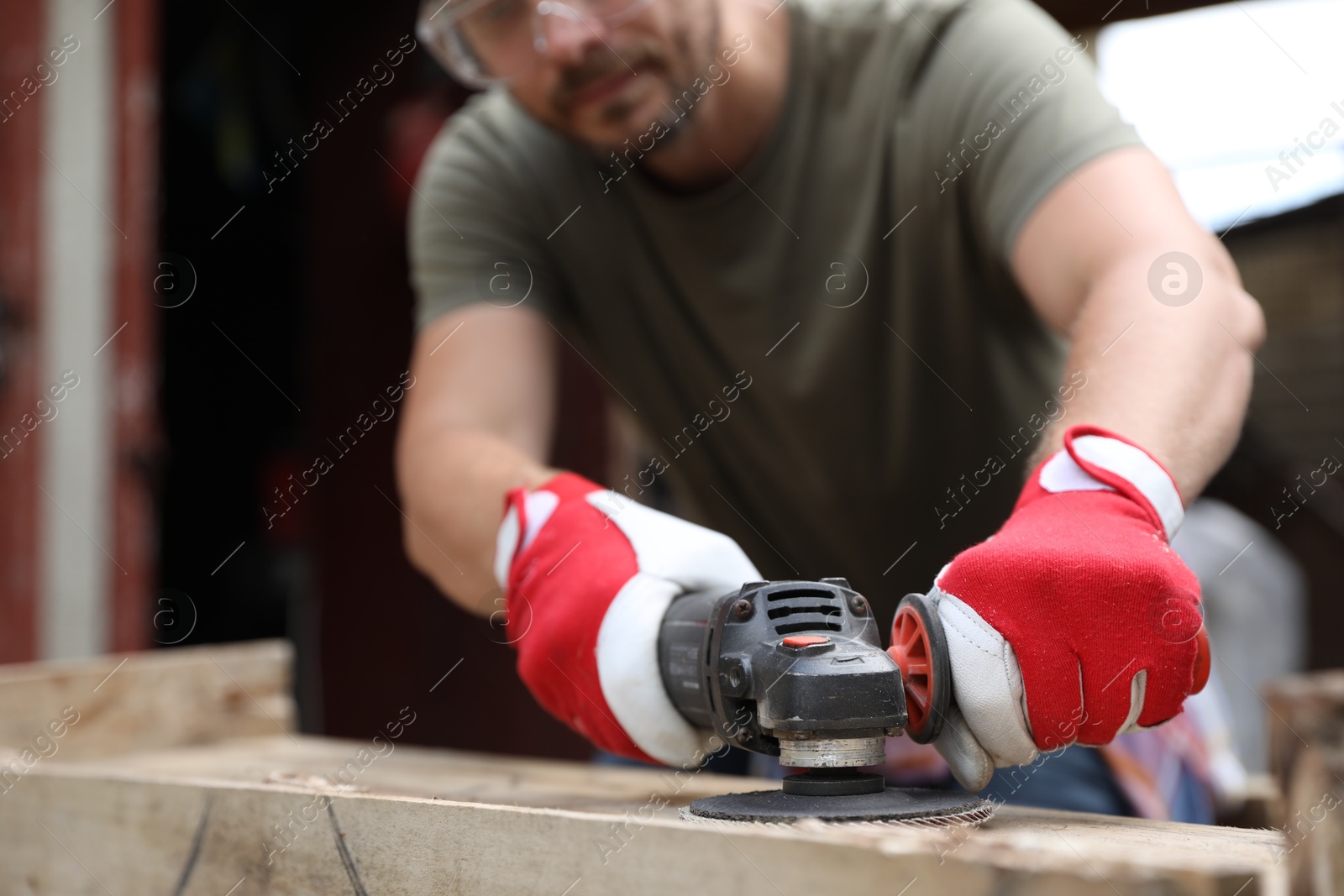 Photo of Man polishing wooden planks with angle grinder outdoors, closeup