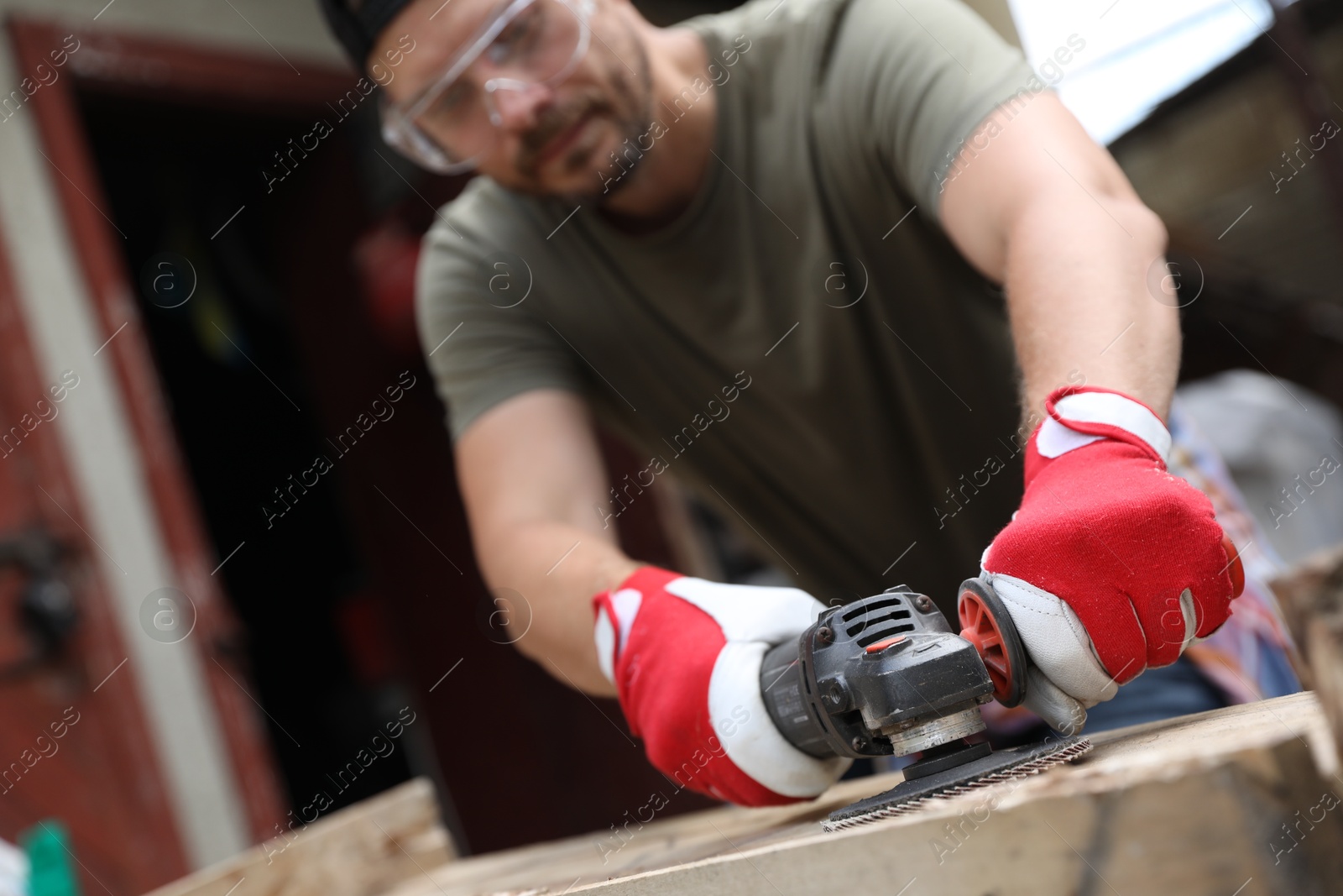 Photo of Man polishing wooden planks with angle grinder outdoors, selective focus