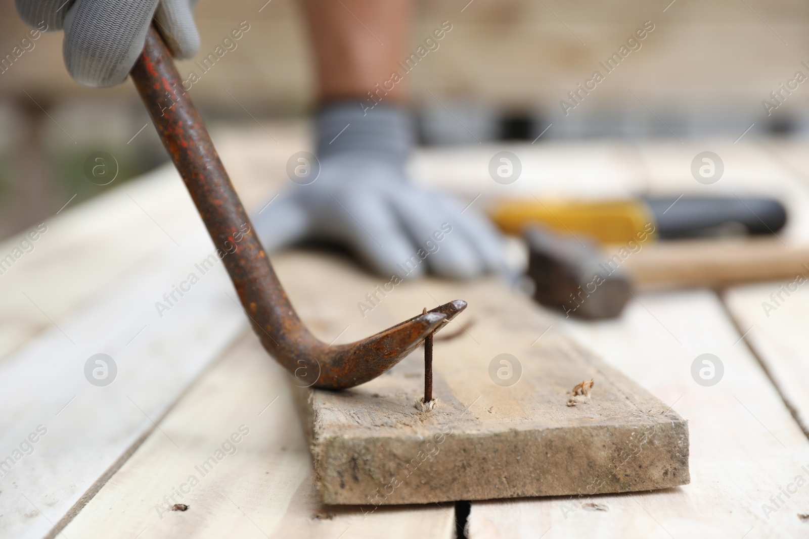 Photo of Man pulling metal nail out of wooden plank with crowbar outdoors, closeup