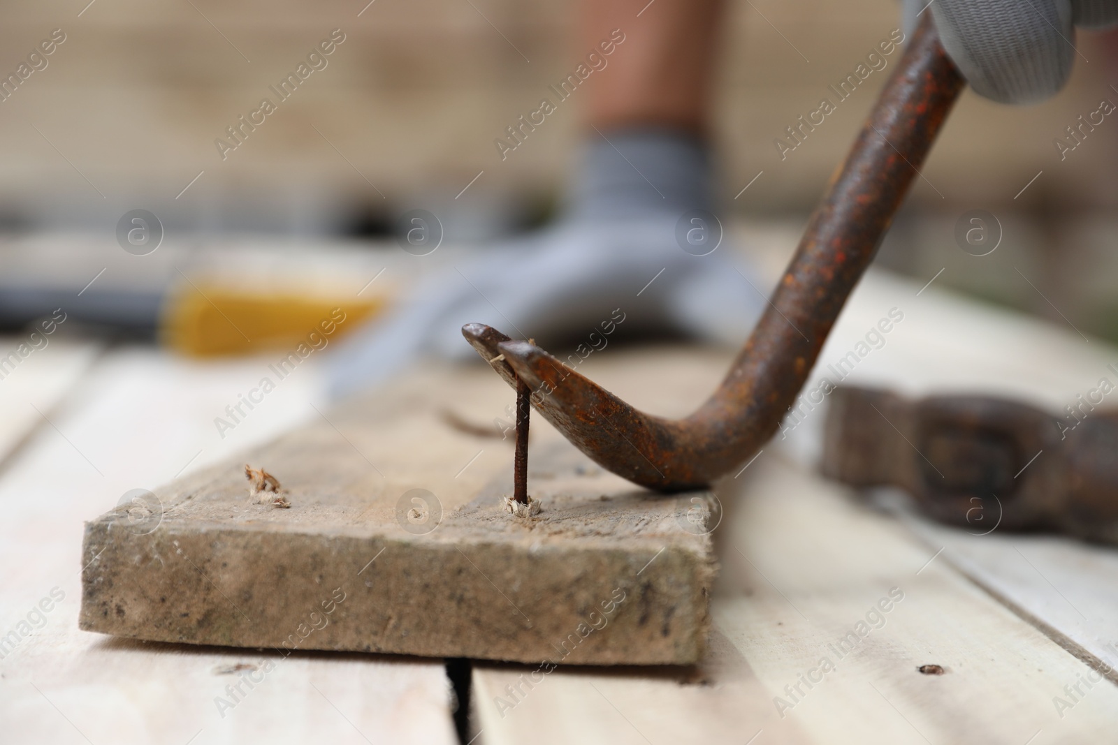 Photo of Man pulling metal nail out of wooden plank with crowbar outdoors, closeup