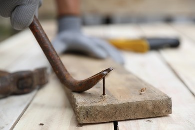 Photo of Man pulling metal nail out of wooden plank with crowbar outdoors, closeup