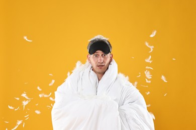 Photo of Overslept man with sleep mask wrapped in blanket on orange background