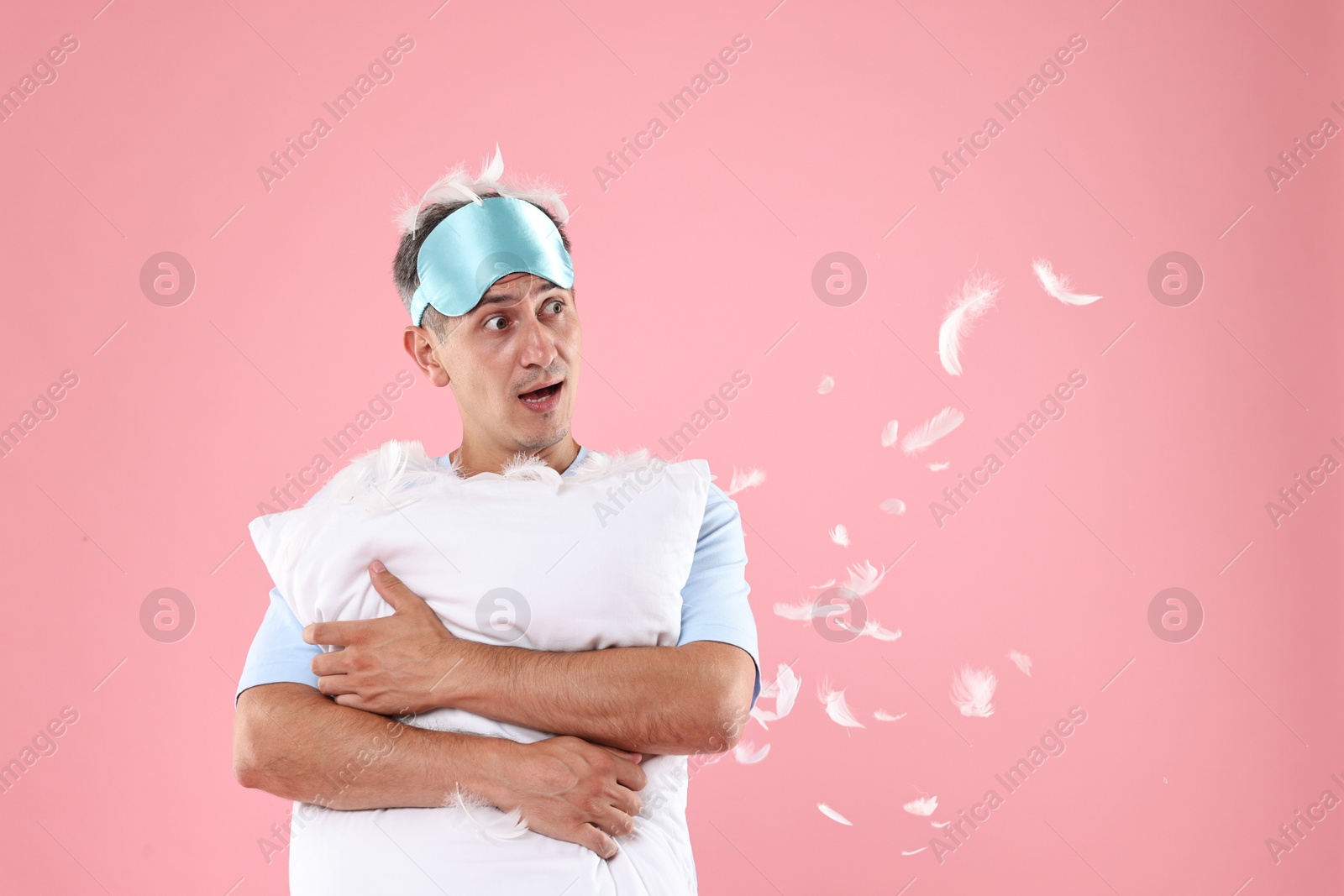 Photo of Overslept man with sleep mask and pillow on pink background