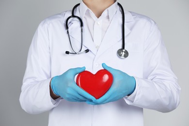 Doctor with red heart on grey background, closeup