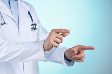 Photo of Doctor pointing at something on light blue background, closeup