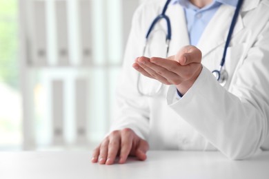 Doctor holding something at white table in clinic, selective focus. Space for text