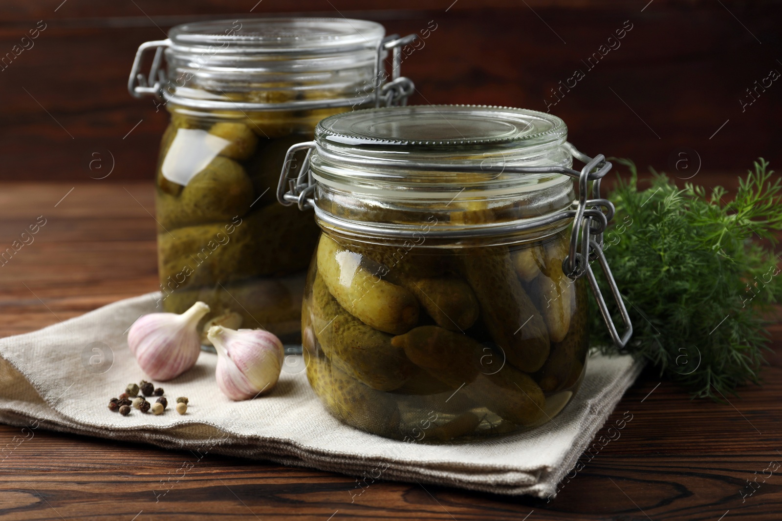 Photo of Pickled cucumbers in jars, garlic, dill and peppercorns on wooden table, closeup